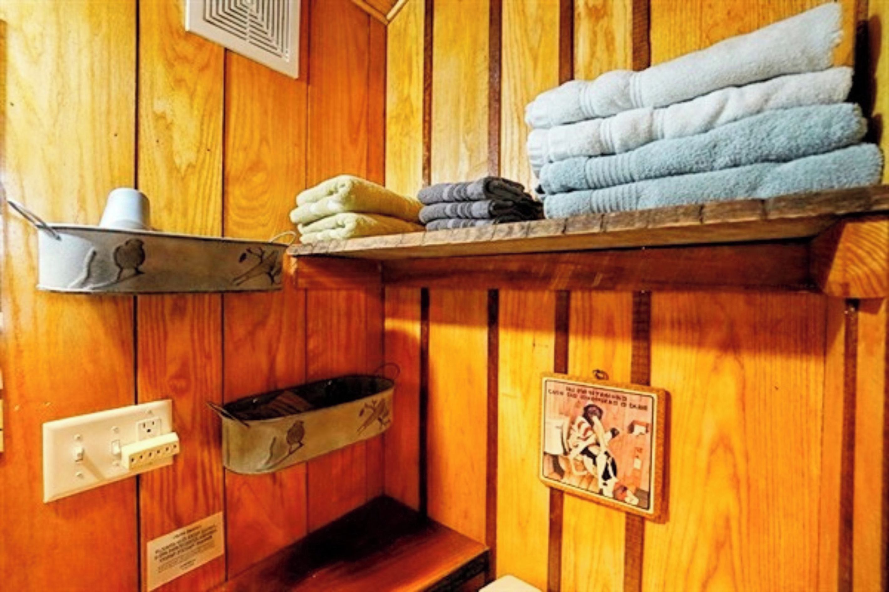 A wooden interior with a shelf holding towels and a small shelf with a cup.