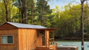 Een houten chalet met een metalen dak, een veranda en een hottub aan een meer.