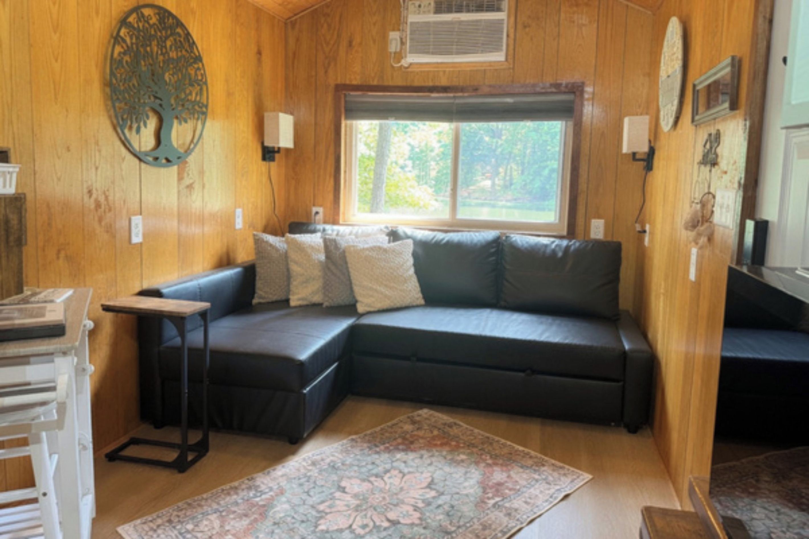 Un intérieur de chalet chaleureux avec un canapé d’angle, une petite table et une grande fenêtre.