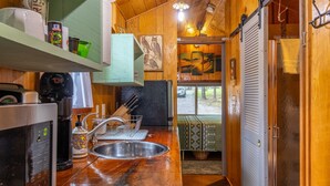 Een compacte keuken met een spoelbak, een koffieapparaat en een magnetron. Er is een houten aanrecht en een deur naar een douchegedeelte.