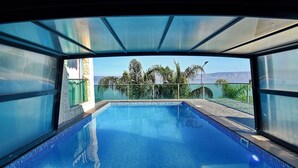 A clear view of a swimming pool with a glass ceiling, surrounded by palm trees and a mountain in the background. - luxury suites (Tiberias)