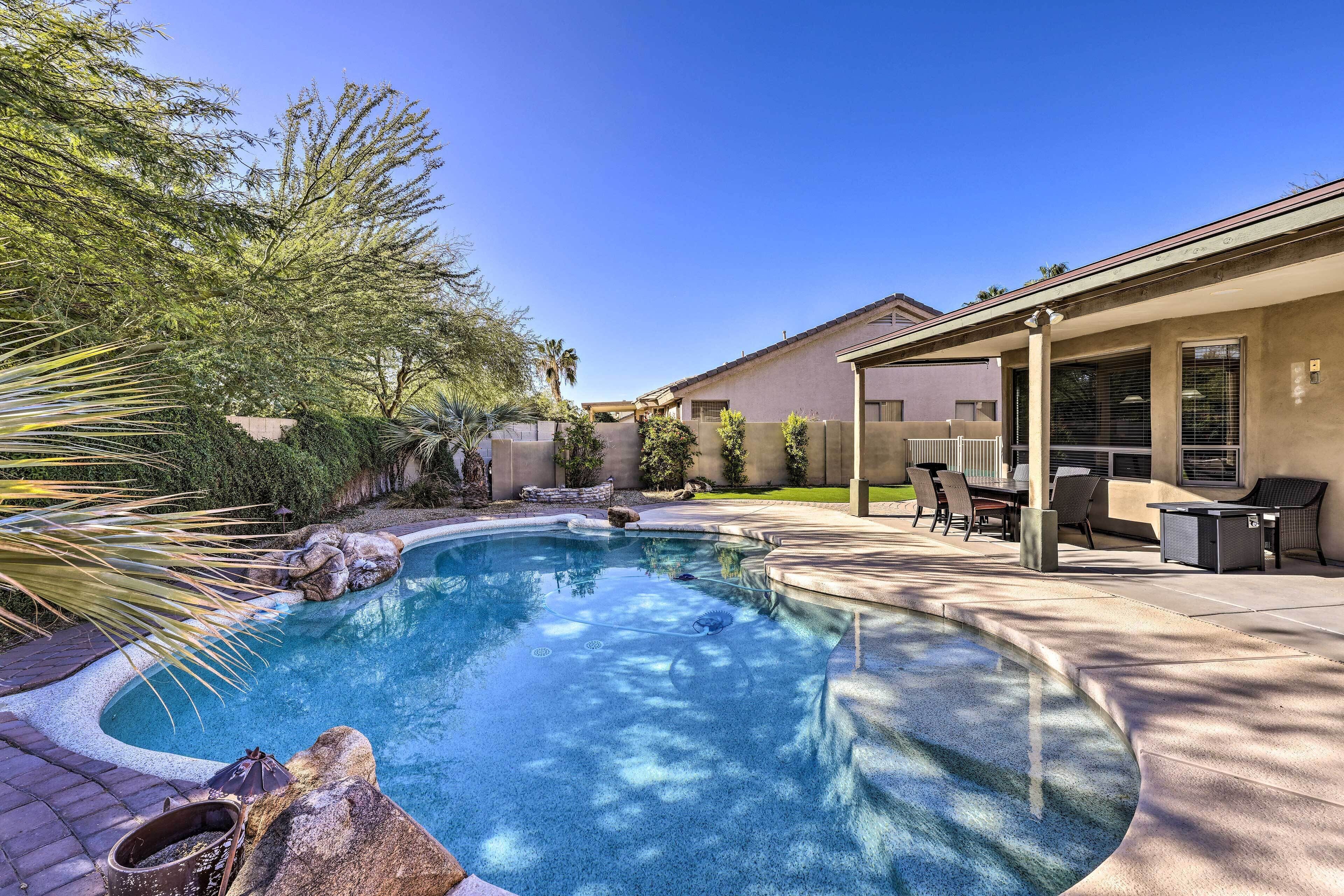Une piscine bordée de pierres, entourée d’une terrasse aménagée avec du mobilier d’extérieur et dotée d’un espace couvert.