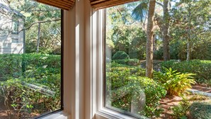 Vista attraverso una finestra con soffitto in legno, su un giardino curato e ricco di piante e alberi.