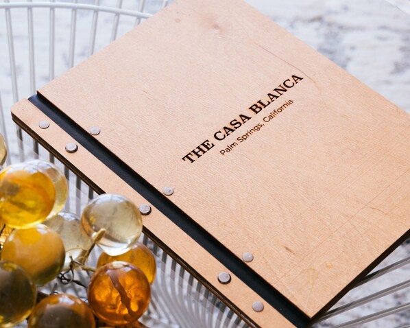 A wooden notebook titled "THE CASA BLANCA Palm Springs, California" with a metal wire basket containing grapes.