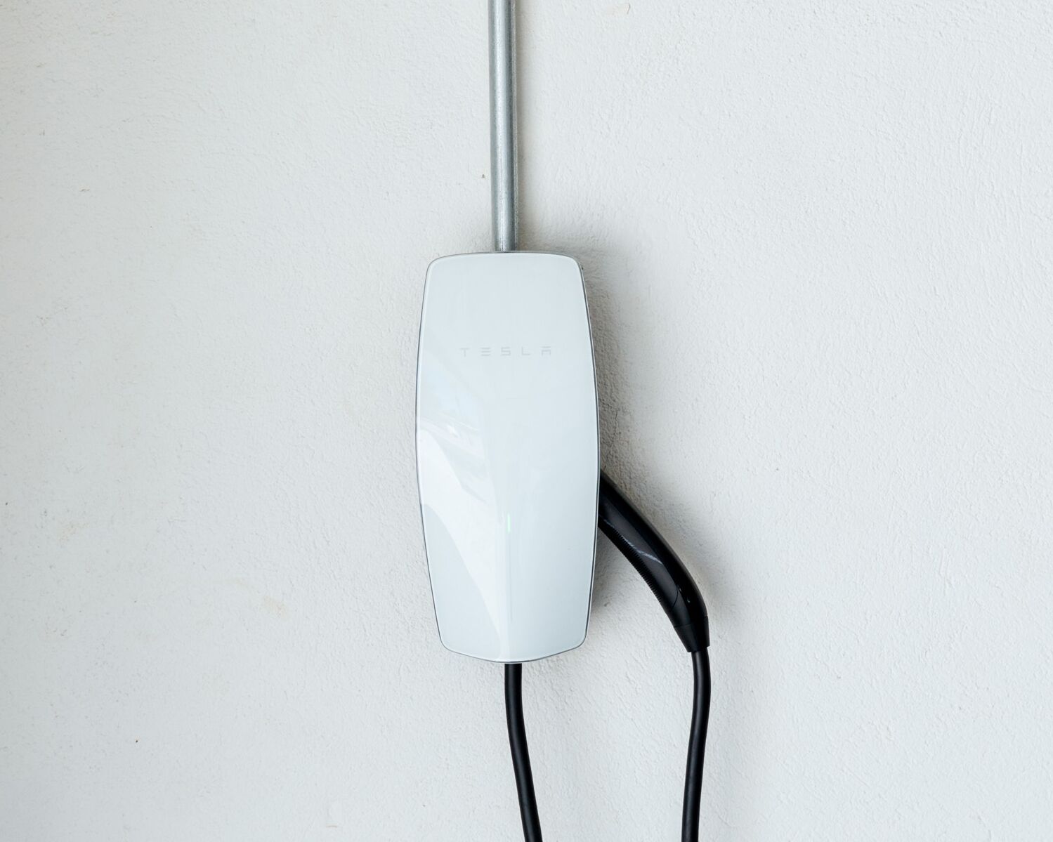 A white Tesla charging station with a cable connected to a metal pole.