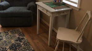Ett rum med en grå fåtölj, en vit stol, ett litet bord med en vävd bordsduk och en mönstrad matta på ett trägolv.