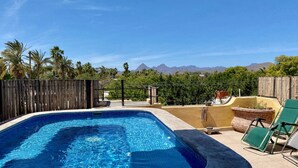 Una piscina rettangolare con acqua cristallina, circondata da una recinzione in legno e da un solarium in cemento.