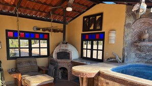 Area esterna rustica con forno in mattoni, vasca idromassaggio, panchina in legno e finestra con vetri colorati.