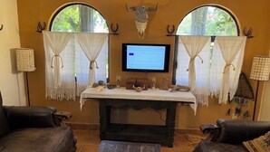 Una stanza con due divani in pelle, un tavolo di legno con oggetti decorativi, una TV a parete e due finestre con tende.