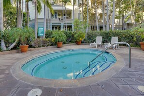 Una piscina con sillones de descanso y plantas en macetas, rodeada por un edificio con balcones.