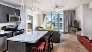 A modern kitchen with granite countertops, stainless steel appliances, and a dining area with a bar stool and red chairs. - 1BD/Austin - Rooftop Pool & Firepit, BBQ! (Austin)