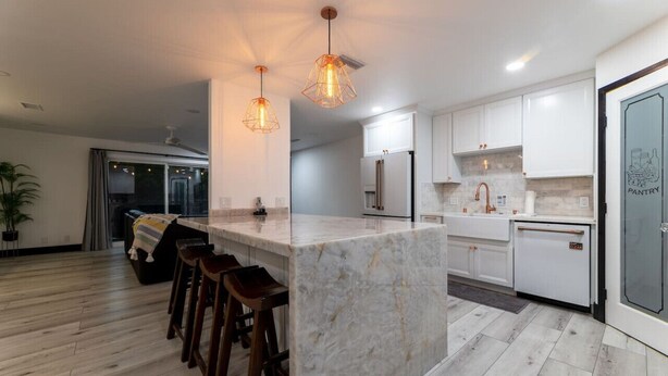 A modern kitchen with white cabinets, a marble island, and pendant lighting.