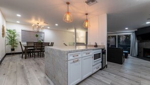 A modern kitchen with white cabinetry, a marble island, pendant lighting, and a dining area with a table and chairs.
