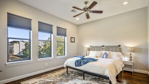 A bedroom with a bed, a ceiling fan, and three windows. - Stoic Sanctuary @ East Downtown (Houston)