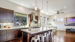 A modern kitchen with dark wood cabinets, a large island with bar stools, and a dining area with a view of the outdoors. - Stoic Sanctuary @ East Downtown (Houston)