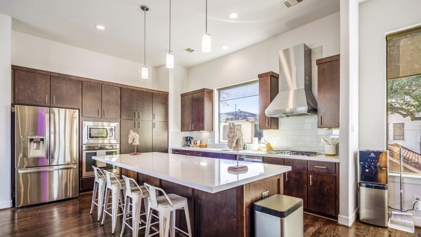 A modern kitchen with a central island, stainless steel appliances, and dark wood cabinetry. - Stoic Sanctuary @ East Downtown (Houston)