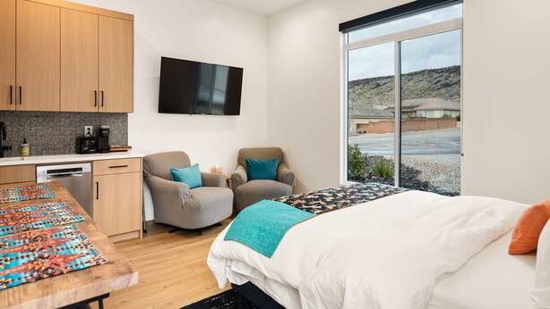 Una habitación de hotel moderna con una cama, un escritorio con un rompecabezas, un televisor y vistas al exterior.
