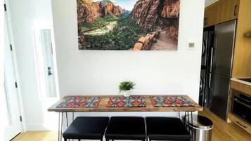 Una cocina moderna con una mesa de madera, taburetes negros y un cubo de basura de acero inoxidable.