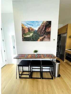 Une cuisine moderne avec une table en bois, des tabourets noirs et une poubelle en acier inoxydable.