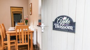 Ruokailutila, jossa on puinen pöytä ja tuolit, pieni maljakko ja kyltti, jossa lukee: ”Apple Blossom Cottage”.