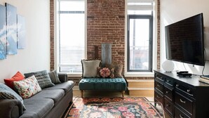 A living room with a brick wall, a sofa, a loveseat, a TV, and a large window. - ✪ Best Apartment in Westport Kansas City ✪ (Kansas City)