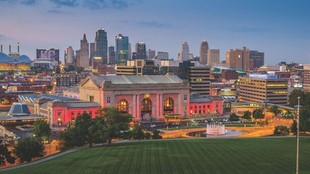 A cityscape with a prominent red building with arched windows and a fountain in the foreground. - ✪ Best Apartment in Westport Kansas City ✪ (Kansas City)
