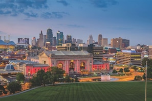 A cityscape with a prominent red building with arched windows and a fountain in the foreground. - ✪ Best Apartment in Westport Kansas City ✪ (Kansas City)