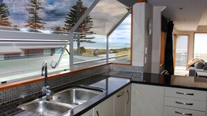 Cocina moderna con un amplio ventanal, pileta de acero inoxidable y alacenas blancas.