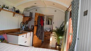 A compact, well-lit room with a kitchenette, a bed, and a bathroom. - Shephards Hut With Hot Tub in the Cotswolds (Stroud)