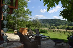 Une terrasse dotée de meubles en osier, d’un barbecue et offrant une vue sur un vignoble.