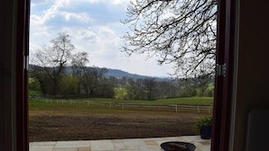 A patio with a table and chair, a fenced field, and trees in the background. - Shephards Hut With Hot Tub in the Cotswolds (Stroud)