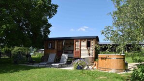 A wooden cabin with a small porch, a hot tub, and a garden with flowers. - Shephards Hut With Hot Tub in the Cotswolds (Stroud)