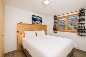 Une chambre à coucher avec une tête de lit en bois, un lit recouvert de draps blancs, un tableau au-dessus du lit et une fenêtre avec des rideaux.