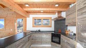 A modern kitchen with wooden cabinetry, a black stove, and a window with a view of the outdoors. - Chalet Amerhone - Luxury Chalet With Jacuzzi (Riddes)