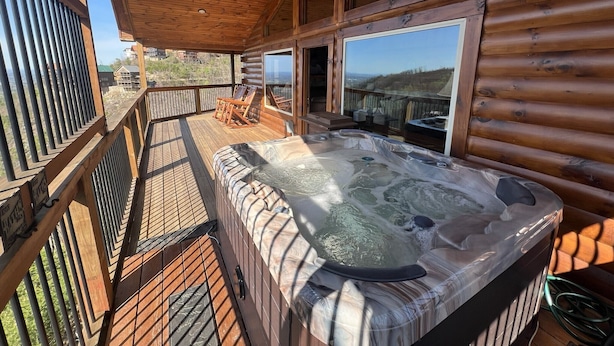 Eine Holzhütte mit Whirlpool, einer Holzterrasse und einer Sitzgelegenheit im Freien.