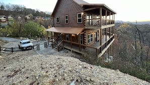Ein mehrstöckiges Blockhaus mit Balkon, gelegen an einem felsigen Hang mit Blick auf umliegende Hütten und Berge.