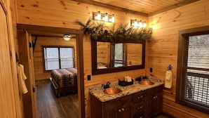 Ein Holzblockhaus-Interieur mit einem Badezimmer, das ein Kupferbecken, Holzschränke und einen Spiegel über dem Becken beinhaltet.
