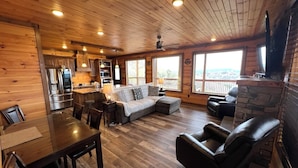 Ein gemütliches Blockhaus-Interieur mit Holzausstattung, einer Essecke, einer Couch, einem Kamin und einer Küche mit modernen Geräten.