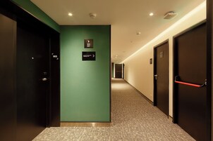 Un pasillo de hotel con señalización direccional, piso alfombrado y puertas con números de habitación.