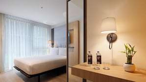 Una habitación de hotel moderna con cama, mesita de noche, espejo, lámpara y una planta en maceta.