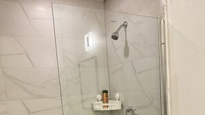 Un baño moderno con cabina de ducha de vidrio, inodoro y repisa con artículos de aseo.
