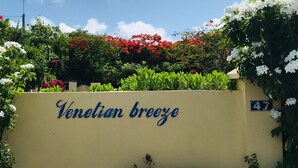 Letrero que dice 'Brisa Veneciana' con el número '47' en una pared, rodeado de abundante follaje y plantas con flores.