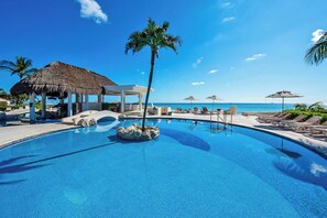 Une piscine entourée de palmiers, avec des chaises longues et des parasols, sous un ciel bleu azur.