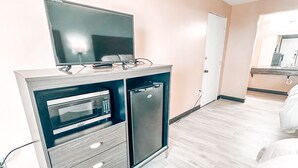 Habitación pequeña con kitchenette que incluye microondas, refrigerador y un televisor de pantalla plana sobre un mueble.
