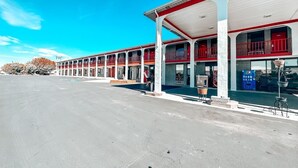 Una estación de servicio con una fila de surtidores rojos y blancos, un amplio estacionamiento y un cielo azul despejado.