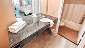 Un baño con lavamanos de mármol, un espejo, un perchero para toallas y una cortina de ducha.