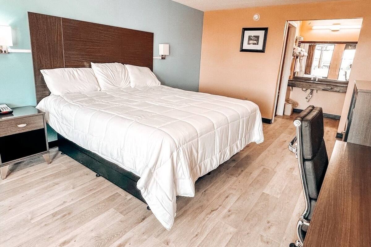 Une chambre d’hôtel avec un lit, une table de chevet, un téléviseur et une salle de bain visible à travers une porte ouverte.