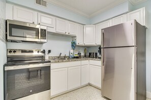 A kitchen with white cabinets, stainless steel appliances including a microwave, oven, and refrigerator, and a speckled floor.