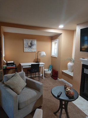 Uma sala de estar com sofá, mesa de jantar com cadeiras, luminária, lareira e um quadro na parede.