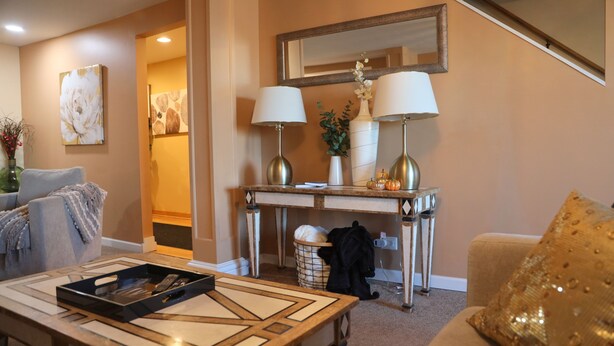 A living room with a sofa, a coffee table with a tray, a console table with lamps, a large mirror, and a decorative vase. - Colorful 4-bedroom house-Vet owned-NAVAL Academy (Waukegan)